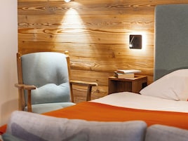 Ein Zimmer mit Holzwänden, einem Bett, einem Sessel und einem Nachttisch mit einem Buch.