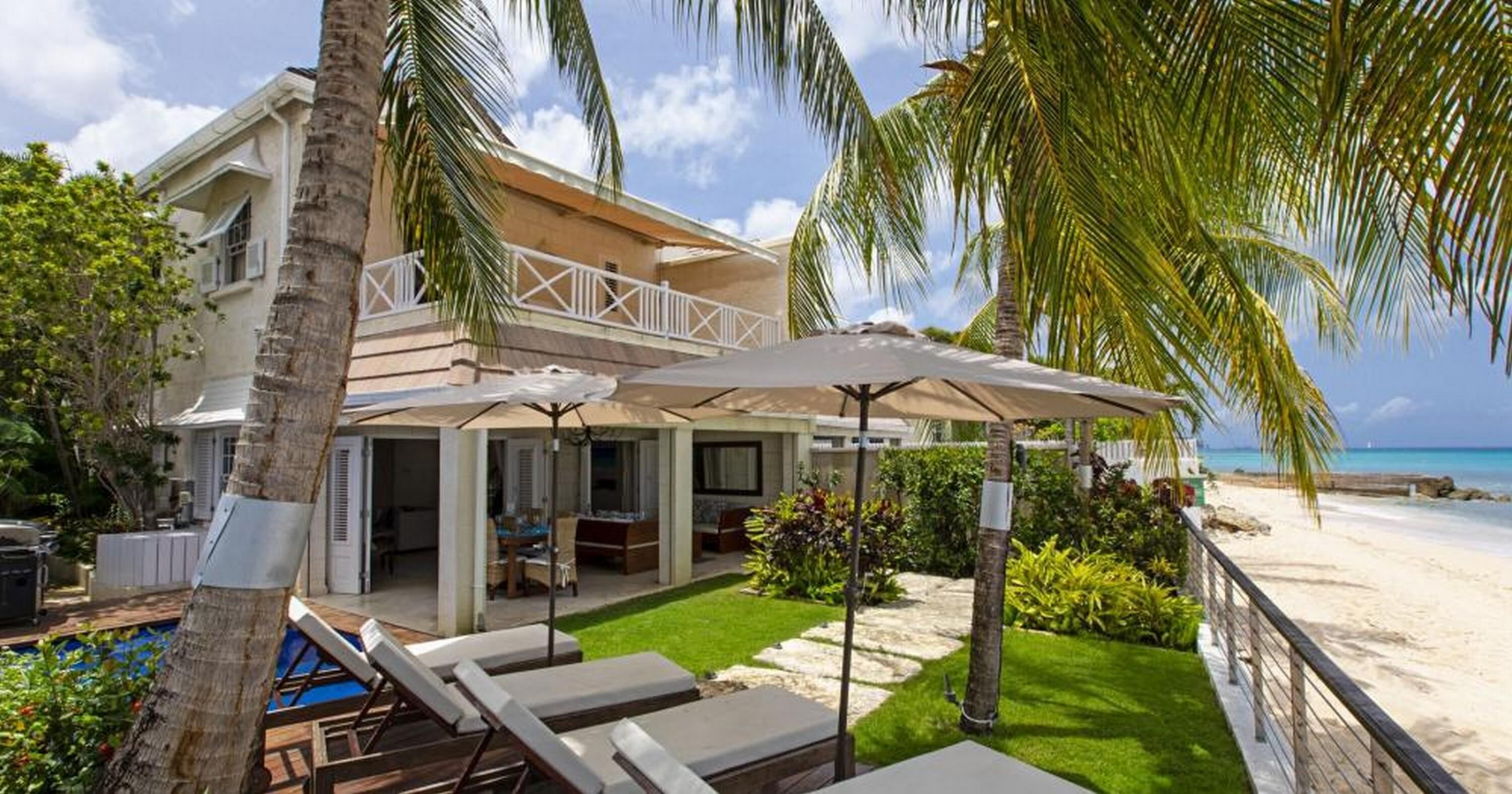 A beachfront property with a covered patio, lounge chairs, and a swimming pool.