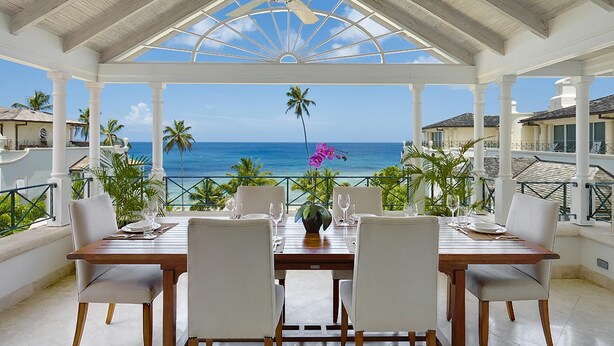 Un área de comedor techada con una mesa dispuesta para seis personas, con vistas a un paisaje marino.