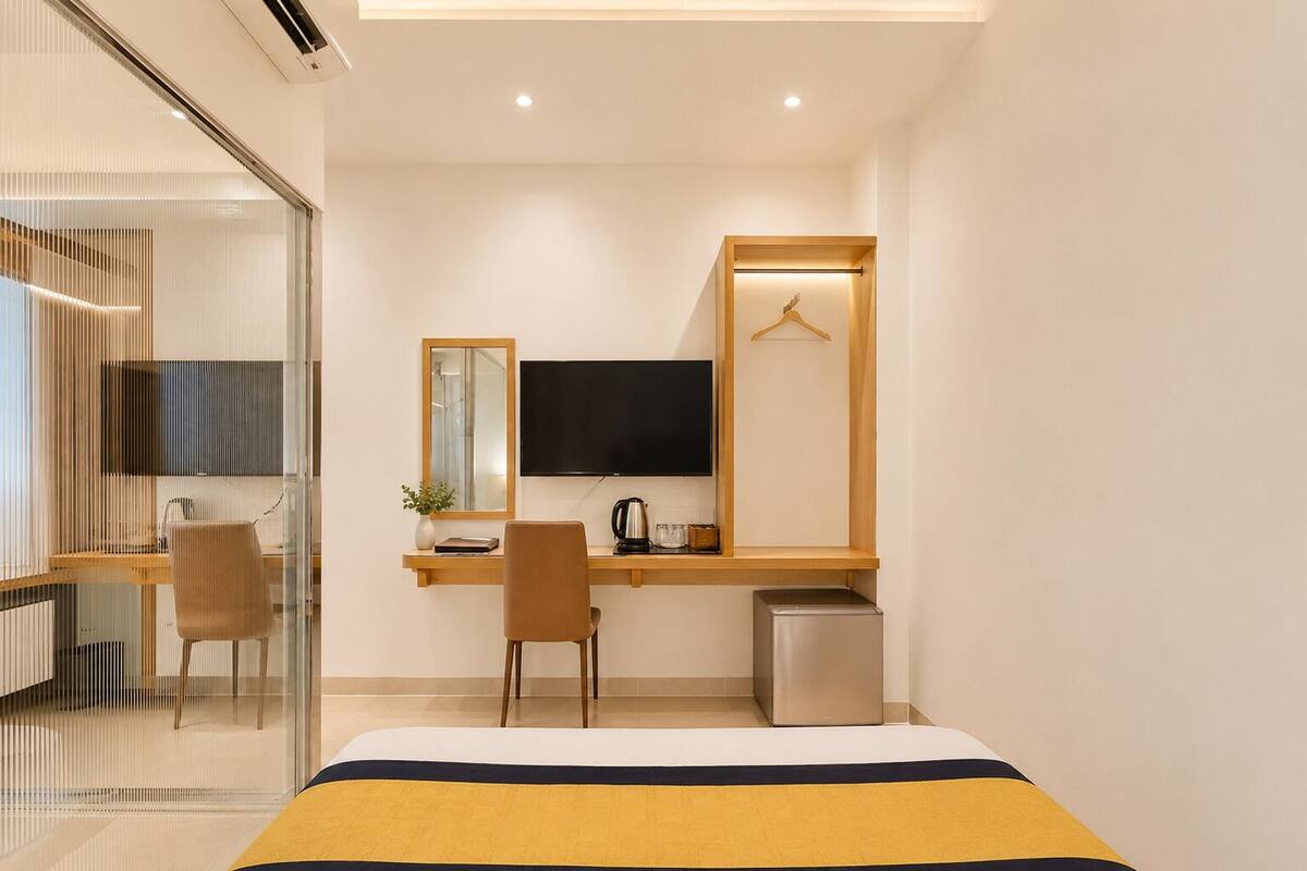 Una habitación de hotel moderna con cama, escritorio con televisor, una silla y una pequeña cocina.