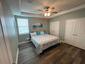 Une chambre à coucher avec un lit, un ventilateur de plafond, un tableau et une armoire.