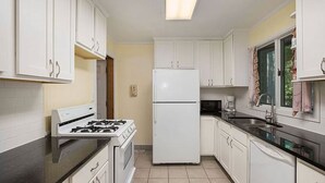 Una cocina con armarios blancos, un refrigerador blanco, una estufa y un fregadero.