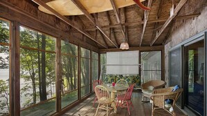 Una terraza de madera con una mesa y sillas, ventanas amplias y un ventilador de techo.