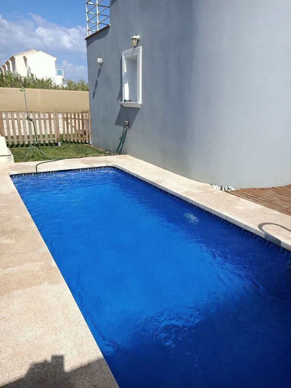A rectangular swimming pool with a blue interior, surrounded by a concrete deck and a wooden fence. - A small house with a private pool (Oliva)