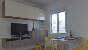 Et moderne køkken med hvide skabe, et fjernsyn og et spiseområde med gule stole og et bord.