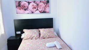 Et soveværelse med seng, et natbord, en vægmonteret aircondition og et blomsterbillede over sengen.