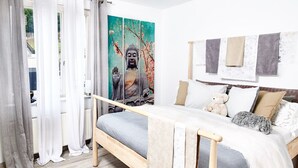 A bedroom with a bed, curtains, a painting of a Buddha, and a view of a garden. - Lo Exclusive Stuttgart - Cozy and central apartment with garden (Stuttgart)