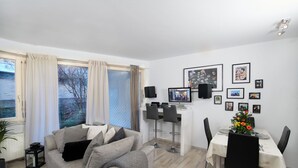 A modern living room with a sofa, a dining table set for two, and a large window with curtains. - Lo Exclusive Stuttgart - Cozy and central apartment with garden (Stuttgart)
