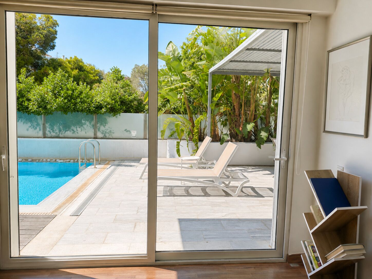 A room with a sliding glass door leading to a pool area with lounge chairs and a pergola.