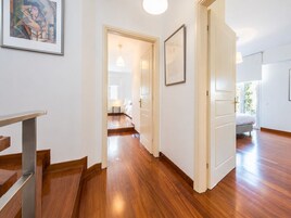 Un pasillo con piso de madera, una escalera y una puerta que da a un dormitorio.