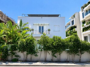 A modern two-story building with a balcony, surrounded by lush greenery and a clear blue sky. - Welcome to Lumen Villa the First of the Adelos Trilogy (Elliniko-Argyroupoli)