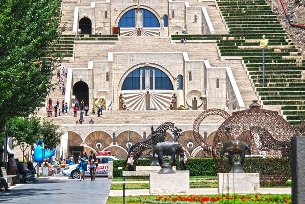 A large public building with a grand entrance, steps leading up to it, and a statue of an elephant in the foreground. - Top of the cascade (Yerevan)