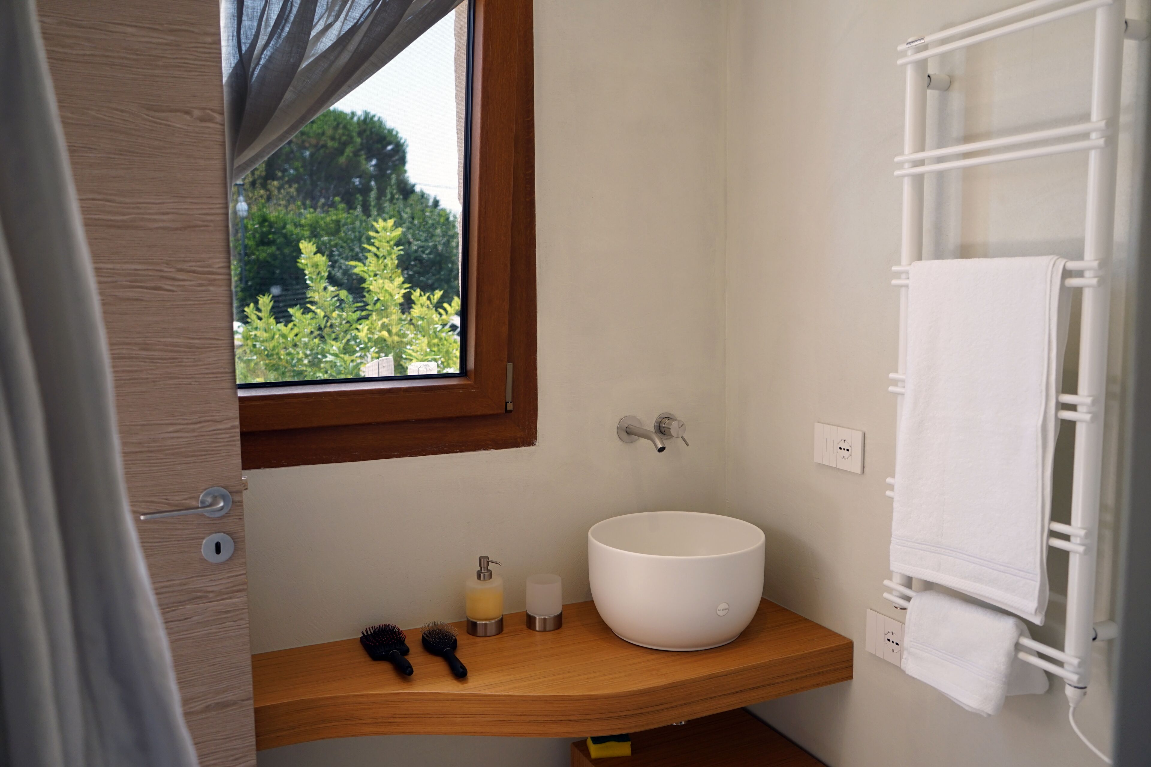 A bathroom with a wooden vanity, a white sink, a window with a view of greenery, and a towel rack.