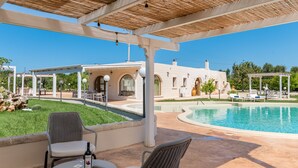 A poolside area with a covered seating area, a pool, and a building with arched windows. - Hasamami Luxury Villa in Ostuni, 4 double bedrooms, private pool  (Ostuni)