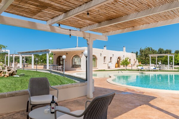 A poolside area with a covered seating area, a pool, and a building with arched windows.