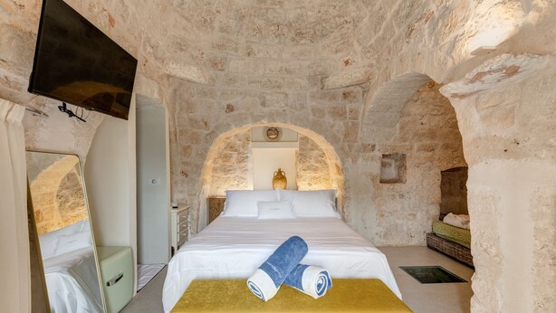 A stone-walled bedroom with a bed, a bench, and a TV mounted on the wall. - Hasamami Luxury Villa in Ostuni, 4 double bedrooms, private pool  (Ostuni)