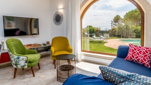 A modern living room with a large window, a flat-screen TV, a green armchair, a yellow armchair, and a blue sofa with patterned pillows. - Hasamami Luxury Villa in Ostuni, 4 double bedrooms, private pool  (Ostuni)