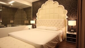A bedroom with a large bed, a nightstand with a lamp, a dresser, and a bathroom with a bathtub and mirror.