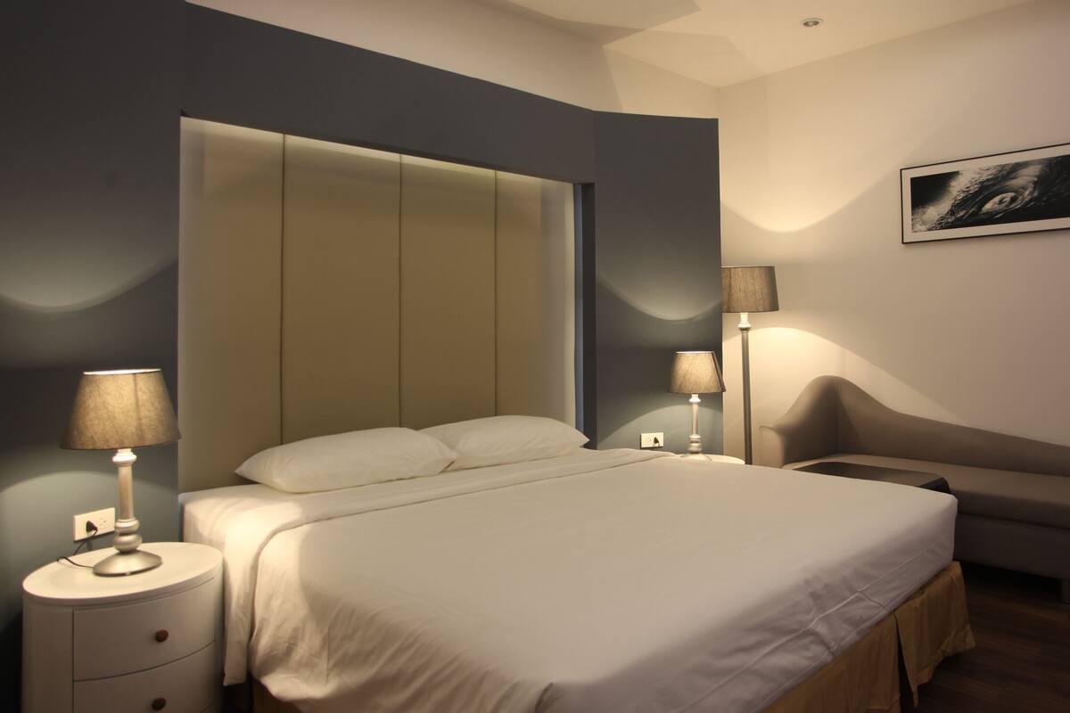 A modern bedroom with a large bed, bedside lamps, a nightstand, a sofa, and a framed picture on the wall.