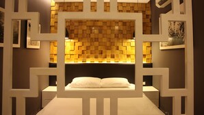 A modern bedroom with a geometric wall design, a bed centered in the room, and framed artwork on the walls.