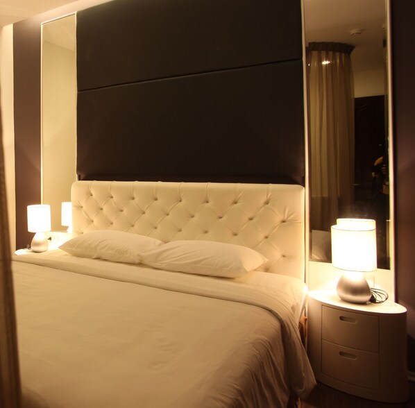 A neatly made bed with a tufted headboard, two bedside lamps, and a nightstand with drawers.