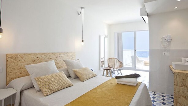 A modern hotel room with a large bed, a small table, and a chair. There is a balcony with a view of the sea. - BJ Cala Morlanda Estudios (Manacor)