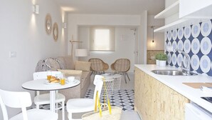 A modern kitchen with a white countertop, a sink, and a patterned backsplash. There is a dining area with a round table and chairs, and a sofa in the background. - BJ Cala Morlanda Estudios (Manacor)