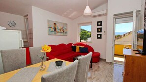 Un espacio habitable compacto con zona de comedor, un sofá rojo, un cuadro y vistas por una ventana.