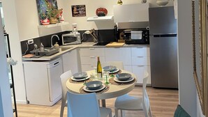 A modern kitchen with white cabinetry, a dining area with a round table, and a staircase leading to an upper level. - Maisonnette (Wintzenheim)
