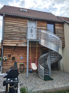 A wooden house with a spiral staircase, a swing, and a grill outside.