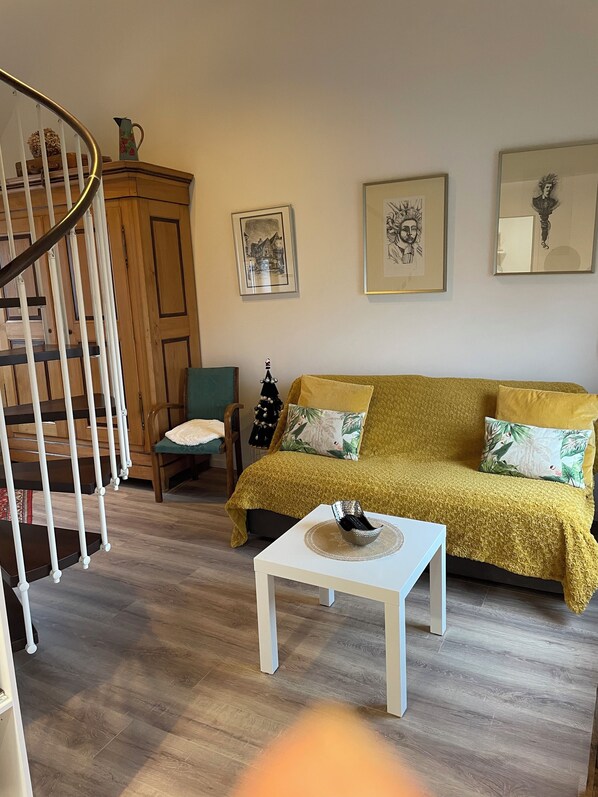A living room with a staircase, a sofa, a coffee table, and framed artwork on the wall.