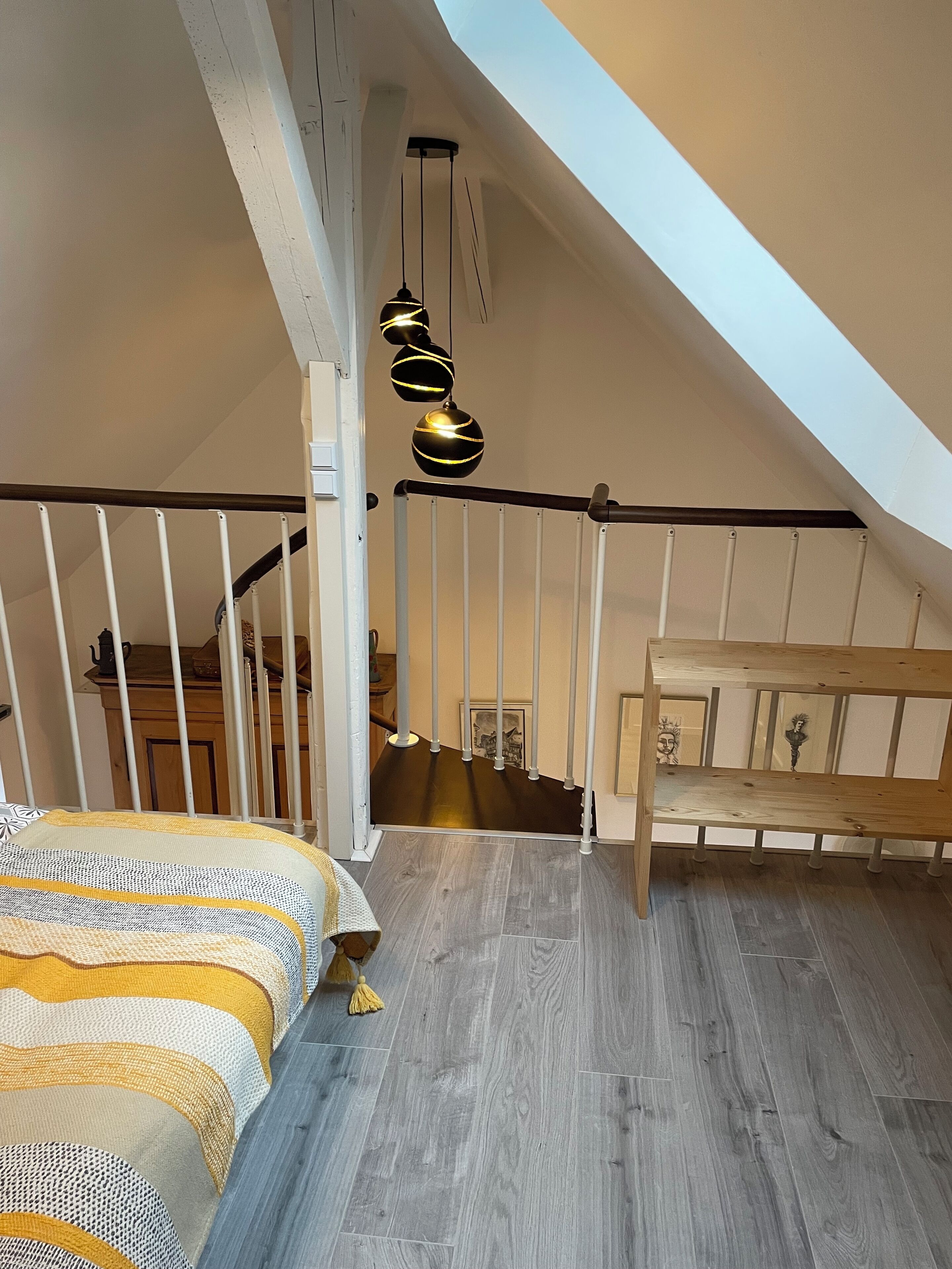 A bedroom with a sloped ceiling, a wooden bench, a bed with a patterned blanket, and a hanging light fixture.