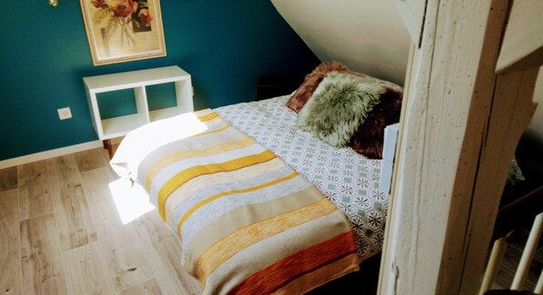A bedroom with a bed, a white nightstand, a wall-mounted shelf, and a painting. - Maisonnette (Wintzenheim)