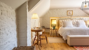 Een slaapkamer met een groot bed, een houten stoel, een klein tafeltje en een lamp.