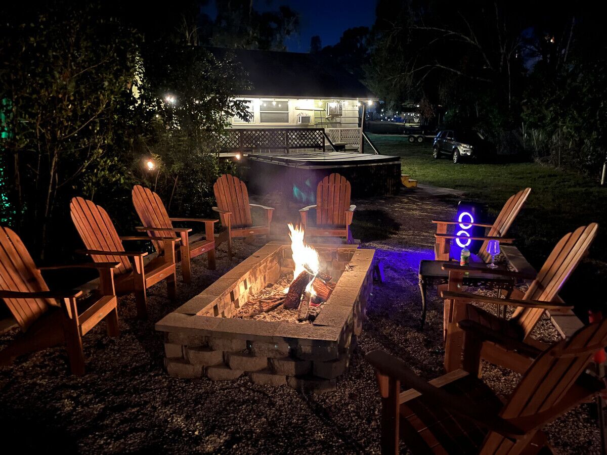 A fire pit with chairs around it, a lit house in the background, and a vehicle parked nearby.
