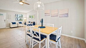 A dining area with a wooden table and white chairs, a ceiling fan, and wall art. - Sweet Home Ponte Verdra: TPC Golf+Park+Outdoor Fireplace+ Nearby Beach Access！ (Ponte Vedra Beach)
