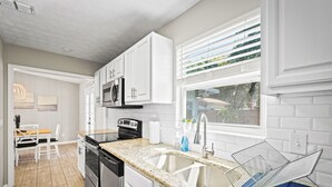 A modern kitchen with white cabinets, a granite countertop, stainless steel appliances, and a large window with blinds. - Sweet Home Ponte Verdra: TPC Golf+Park+Outdoor Fireplace+ Nearby Beach Access！ (Ponte Vedra Beach)