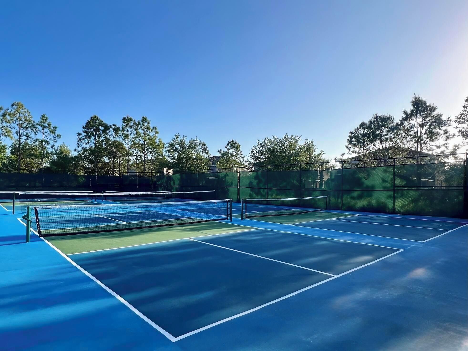 Tenniskenttä, jossa on verkko, ja jonka ympärillä on puita ja aita.