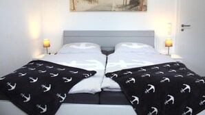 A double bed with a grey headboard, two bedside lamps, and a beach-themed painting above it. - Am Vossgarten apartment 2, terrace, WLAN, underfloor heating, non-smoking, incl. beach chair (Cuxhaven)