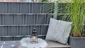 A dark-colored outdoor seating area with a lantern, a patterned cushion, and a fluffy white throw. - Am Vossgarten apartment 2, terrace, WLAN, underfloor heating, non-smoking, incl. beach chair (Cuxhaven)