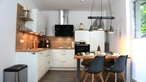 A modern kitchen with white cabinets, a wooden countertop, and a dining area with a table and chairs. - Am Vossgarten apartment 2, terrace, WLAN, underfloor heating, non-smoking, incl. beach chair (Cuxhaven)