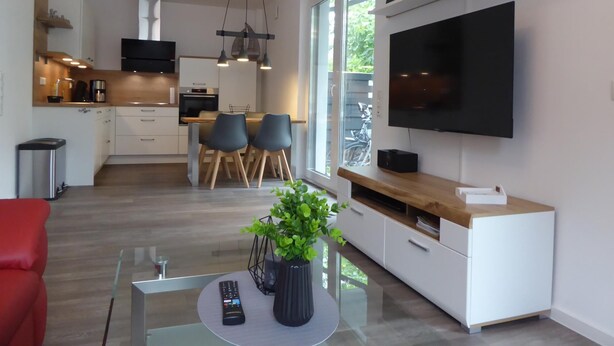 A modern kitchen with a dining area, a TV mounted on the wall, and a small plant on the table. - Am Vossgarten apartment 2, terrace, WLAN, underfloor heating, non-smoking, incl. beach chair (Cuxhaven)