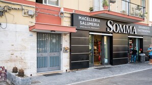 A storefront with 'MACELLERIA SALUMERIA' and 'SOMMA' signs, indicating a specialty food preparation shop. - GuestHost - Roomy and Bright Apartment with Balconies x6 (Catania)