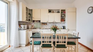 A modern kitchen with white cabinets, a dining table with chairs, and a view of the city through a large window. - GuestHost - Roomy and Bright Apartment with Balconies x6 (Catania)