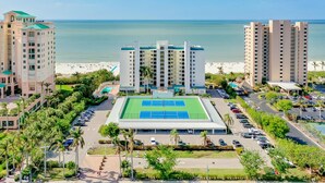 Ett hotellkomplex med flera höga byggnader, en central tenniskort och utsikt över stranden.