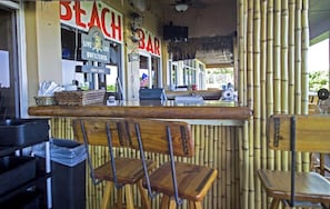 En strandbar med en vägg av bambu, trästolar och en bardisk med en skylt som lyder: ”LEV LIVET ÄKTLIGT”.
