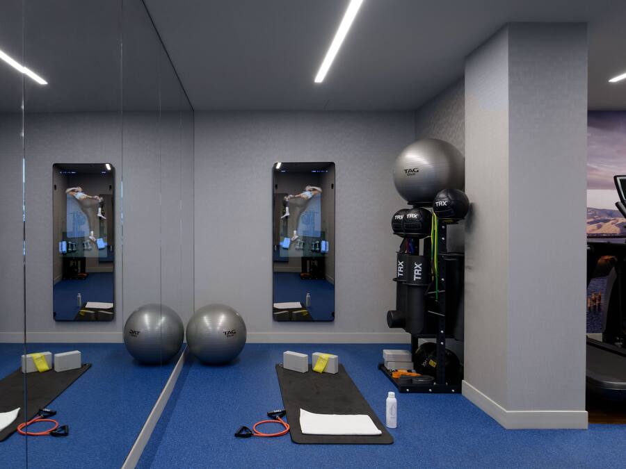Un gimnasio con equipo de ejercicio, cinta de correr y pared espejada.