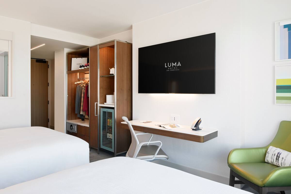Een hotelkamer met een bed, een bureau, een stoel, een kledingkast en een televisie aan de muur.