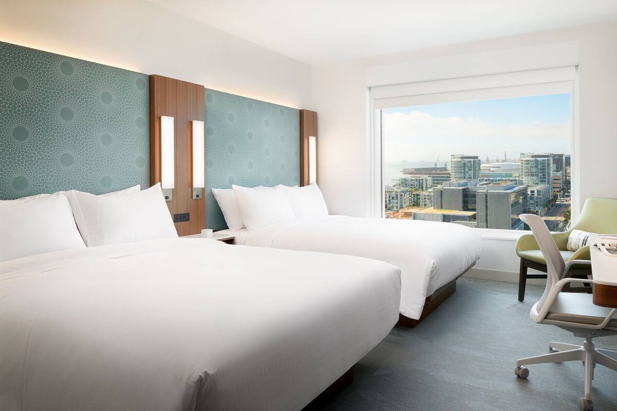Een hotelkamer met twee bedden, een bureau en uitzicht op een stadsbeeld.