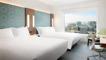A hotel room with two beds, a desk, and a view of a cityscape.